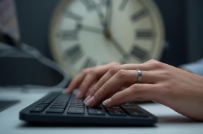una immagine che mostri due mani che lavora al computer con lo sfondo di un orologio